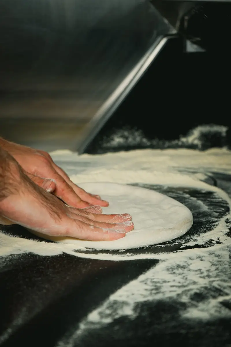 Hands stretching a ball of dough on a floured bench at Drummoyne