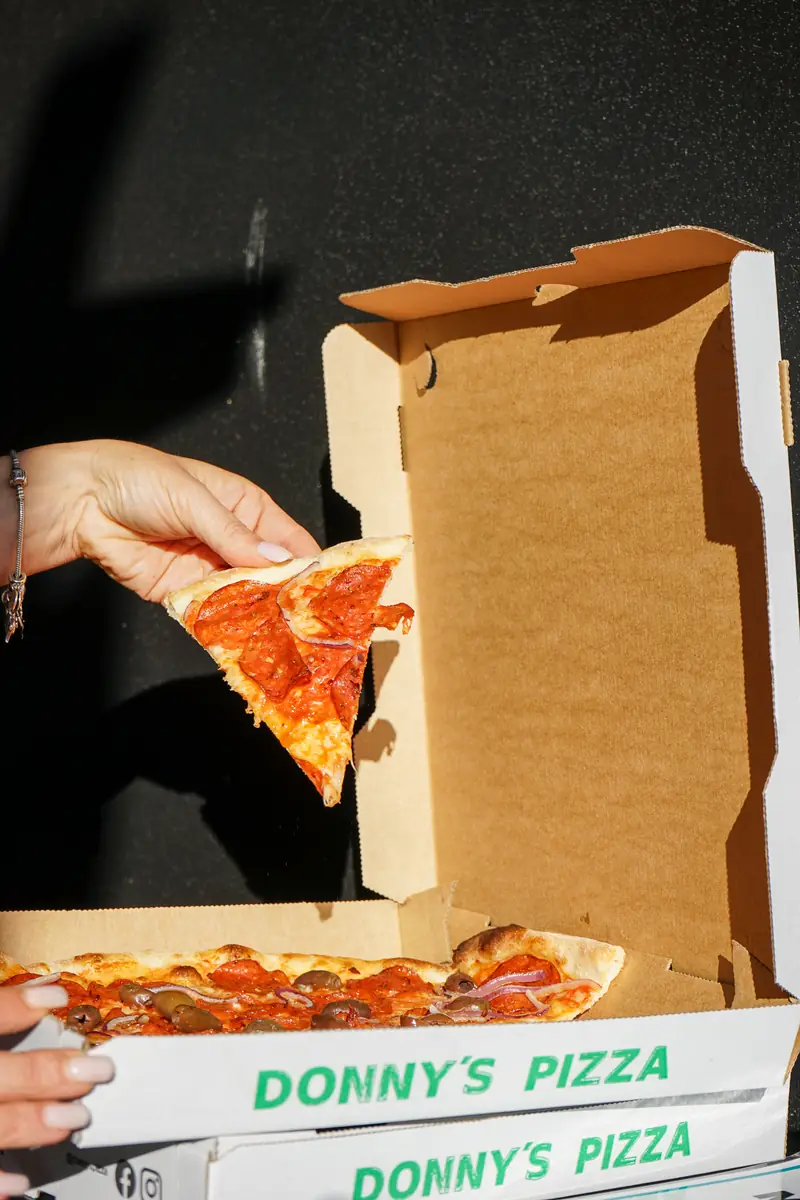 A slice of salami pizza lifted out of a Donny's Pizza box